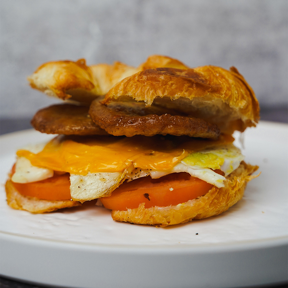 A breakfast sandwich with sausage, tomato, and cheese on a croissant served at our Brooklyn coffee shop.