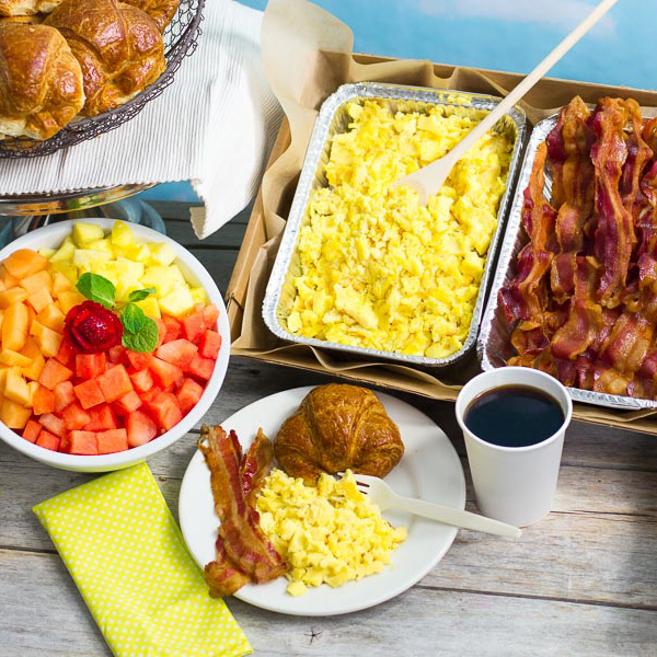 Trays of scrambled eggs and bacon along with a fruit bowl for Dutch Kills, Queens, New York office catering service.