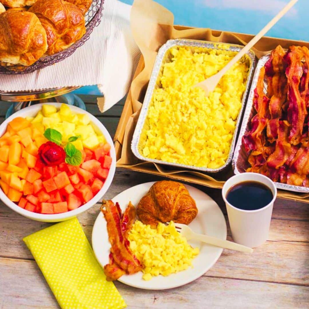 Trays of scrambled eggs and bacon along with a fruit bowl for breakfast catering near Central Harlem NY.